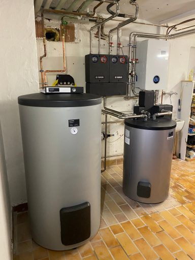 Zwei silberne Wassertanks in einem Kellerraum mit Rohrleitungen und Steuerungseinheit.