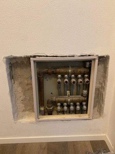 Wandöffnung mit Sicht auf ein Rohrsystem und Ventile hinter einem Rahmen.