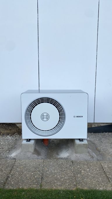 Außenanlage einer Klimaanlage auf Pflastersteinen vor weißer Wand.