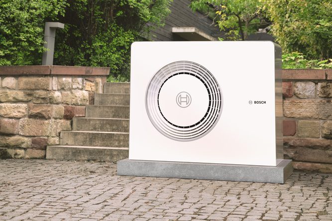 Moderne Luft-Wasser-Wärmepumpe im Außenbereich eines Einfamilienhauses, umgeben von Garten.