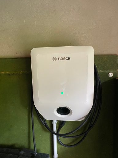 Weißer Bosch-Ladecontroller an der Wand mit einem grünen Statuslicht.