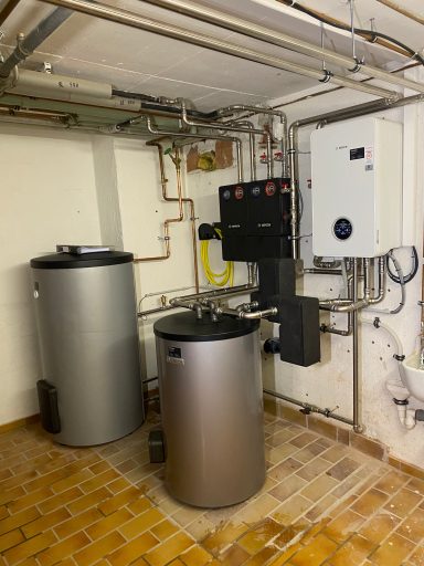 Heizungsanlage mit zwei silbernen Warmwasserspeichern und einem Steuergerät an der Wand.