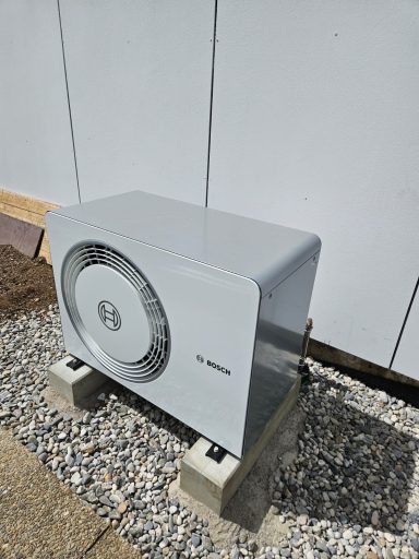 Wandmontierte Klimaanlage auf Betonfundament in einem Außenbereich.