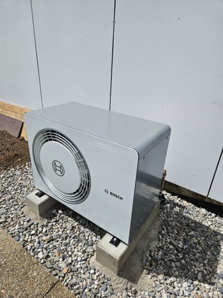 Wandhängende Klimaanlage in silberner Farbe auf einem Betonfundament.